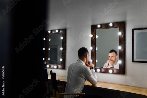 Portrait of handsome young man in white shirt looking into the mirror.