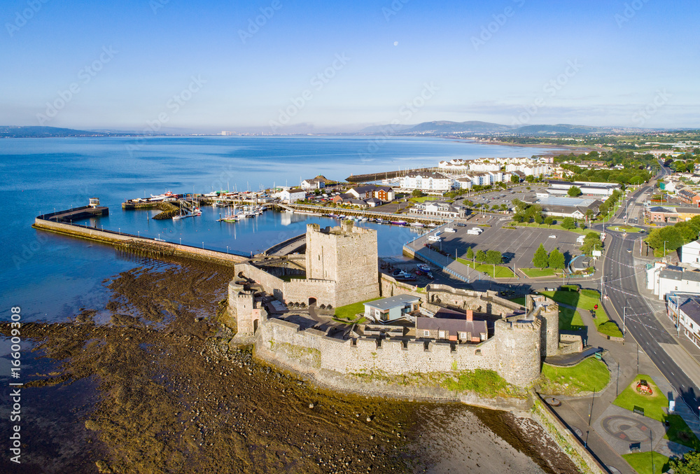 Medieval Norman Castle in Carrickfergus near Belfast in sunrise light. Aerial view with marina, yachts, parking, town and far view of Belfast in the background.
