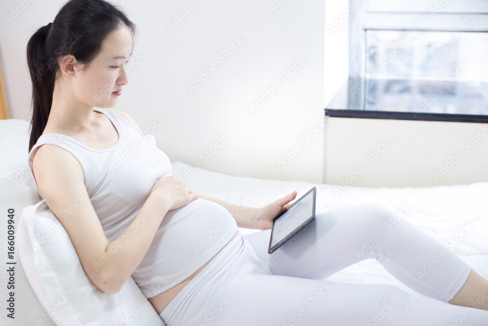 pregnancy, technology, people and expectation concept - close up of pregnant woman with tablet pc computer in bed at home pregnancy, technology, people and expectation concept - close up of pregnant woman with tablet pc computer in bed at home