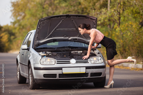 Young woman looks under the hood of her car and trying to find the cause of breakage © artem_goncharov