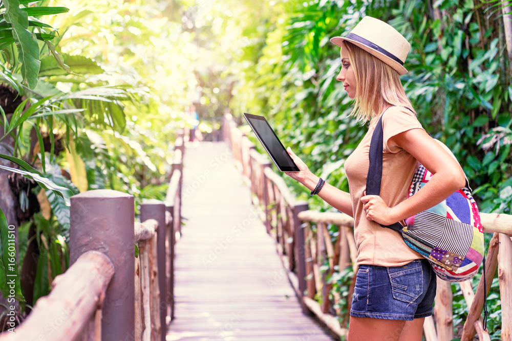 Travelling concept. Technology and adventure. Young woman using tablet computer in jungle.