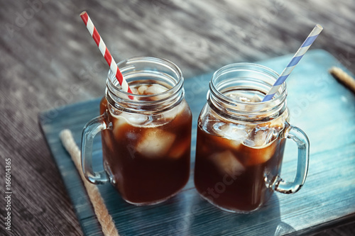 Foto Mason jars with cold brew coffee on wooden tray