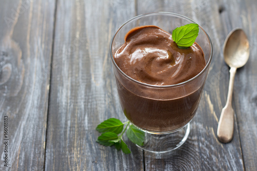 Delicious vegan chocolate mousse with banana, cocoa and mint in glasses on a wooden surface, selective focus