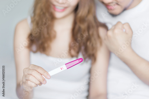 Selective focus happy excited couple for positive pregnancy test in bedroom.