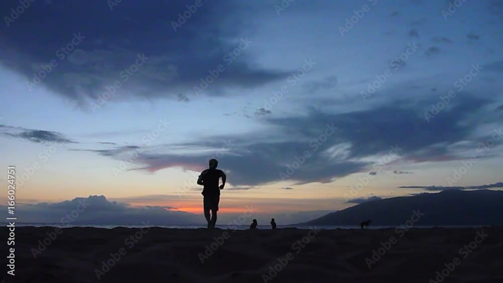 Man running away from camera towards the ocean during evening sunset at the beach in Hawaii.