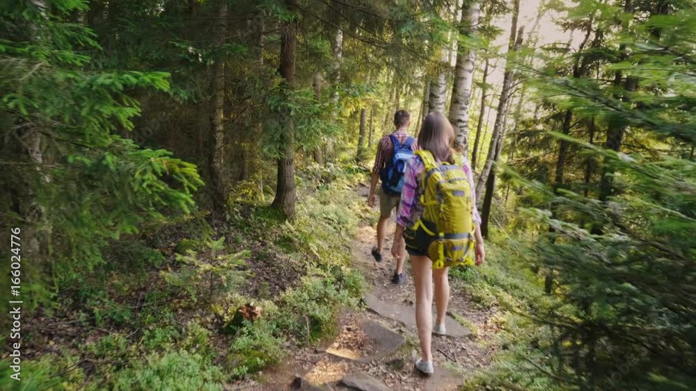Two tourists walk along a narrow picturesque mountain path. The sun shines beautifully before sunset. Adventures and an active way of life