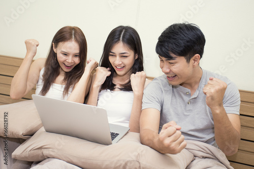 Asian man and woman using computer on bed, Young people portrait in bedroom, people with success emotion, 20-30 years old.