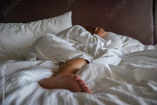 woman in white robe laying in bed covering head in daylight
