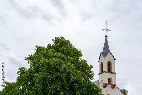 White church tower behind a green tree. Neubamberg, Rhine-Hesse, Germany