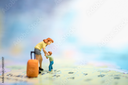 Family and travel concept. Mother and son miniature figures with orange luggage standing, playing, take care child on world map.