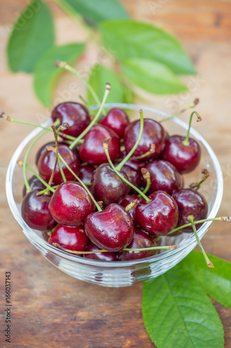 Ripe red cherries with green leaves in a transparent bowl