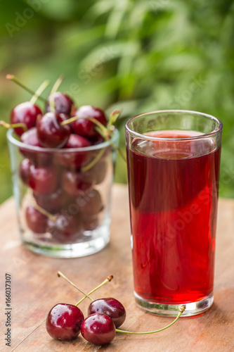 A glass of cherry juice and cherries on the table outdoors