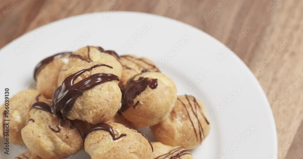 Slow motion fly out shot of profiteroles with fine dark chocolate on plate Slow motion fly out shot of profiteroles with fine dark chocolate on plate
