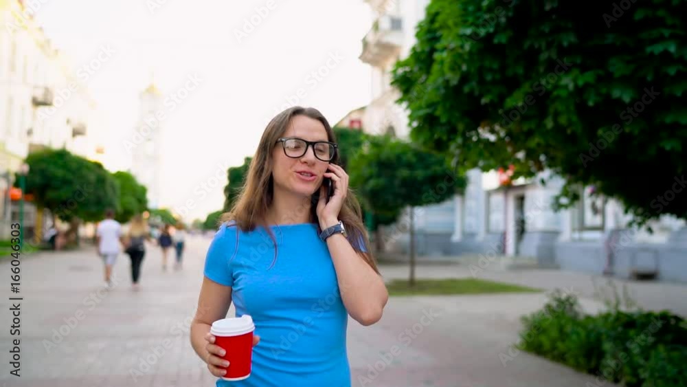 Woman talking on the smartphone and drinking coffee walking down the street