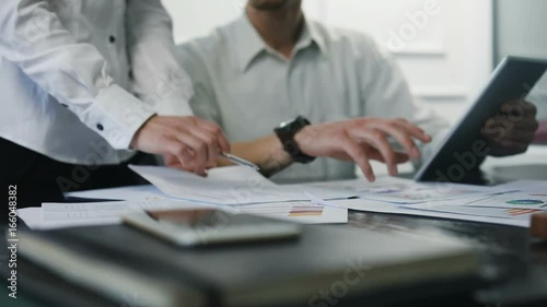 Young and smart businesspeople smiling coworking commenting and showing graphic stats, taking a business conversation in an office interior slow motion