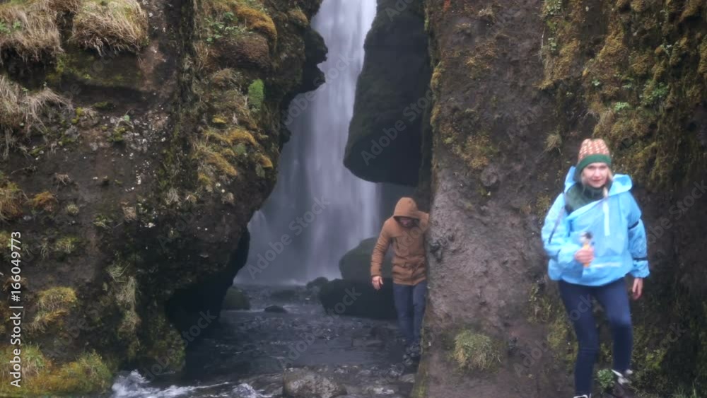 Two young tourists exploring the powerful waterfall Gljufrabui in Iceland. Man and woman in raincoat walking in rain. Two young tourists exploring the powerful waterfall Gljufrabui in Iceland. Man and woman in raincoat walking in rain.
