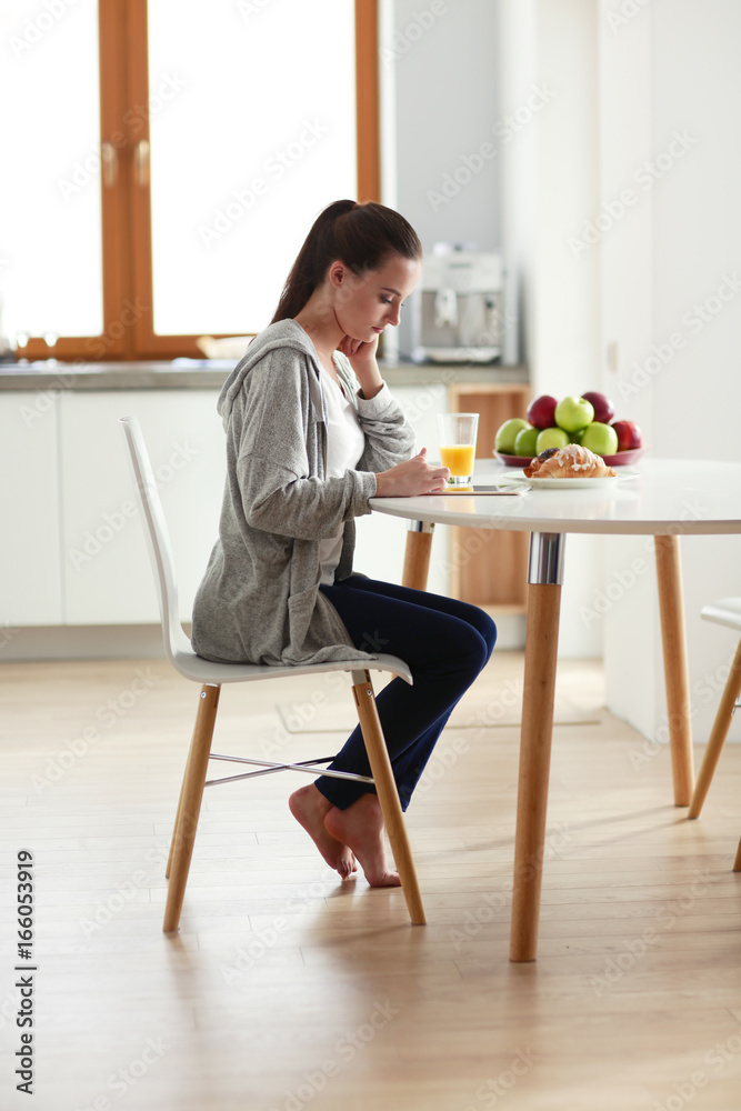 Young woman with orange juice and tablet in kitchen.