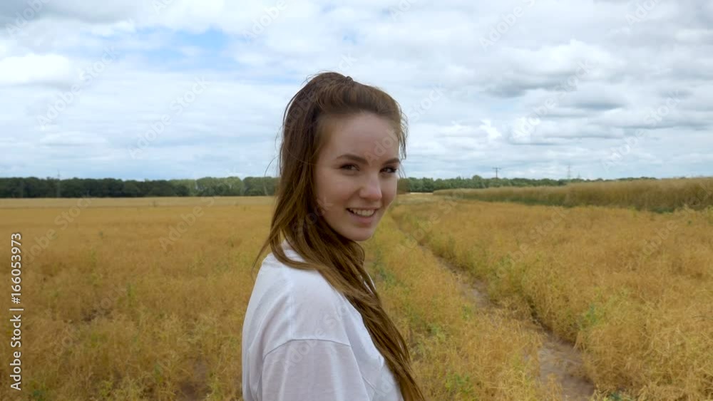 A young woman walks in a grass field towards the camera. Filmed in medium shot with an expansive blue sky and trees in the horizon. A young woman walks in a grass field towards the camera. Filmed in medium shot with an expansive blue sky and trees in the horizon.