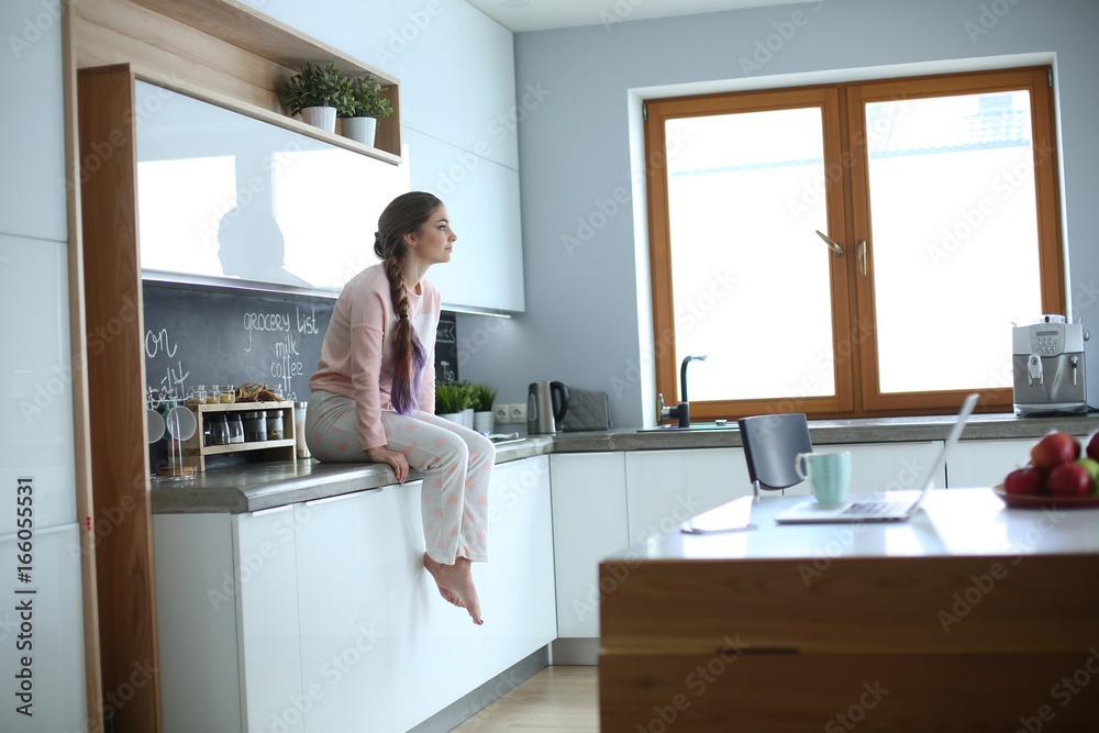 Young woman sitting on table in the kitchen. Young woman sitting on table in the kitchen.