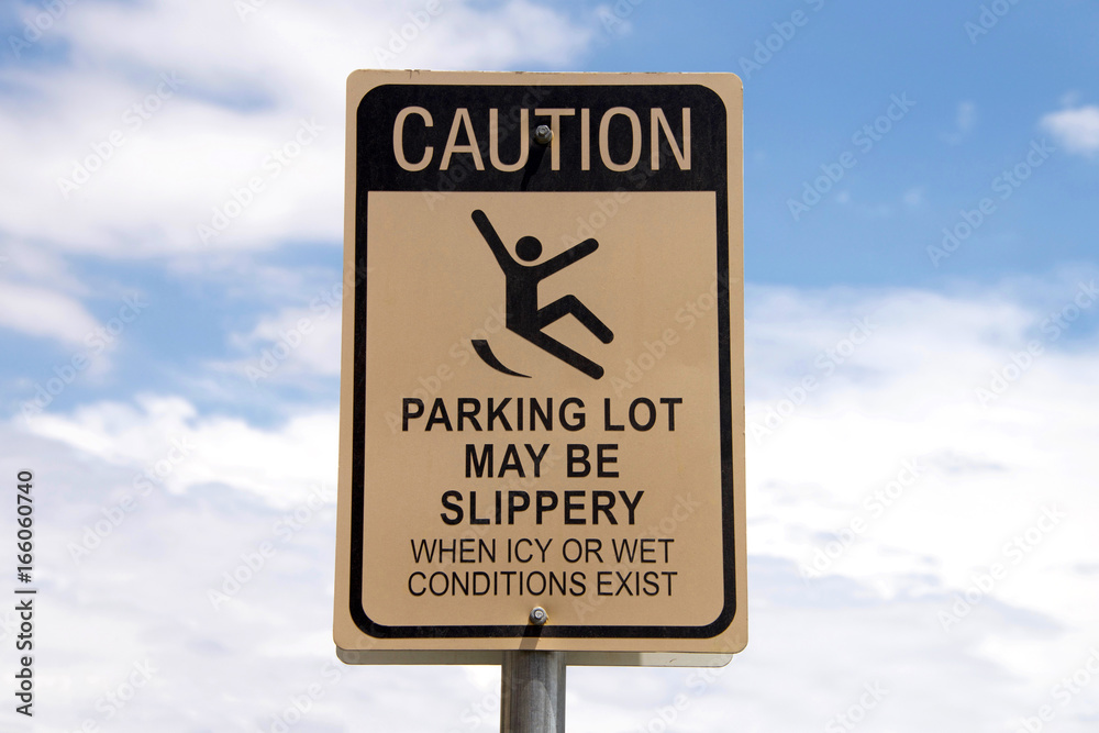 Caution, Slippery when wet sign in a parking lot. Warning patrons. Blue sky with fluffy white clouds in background