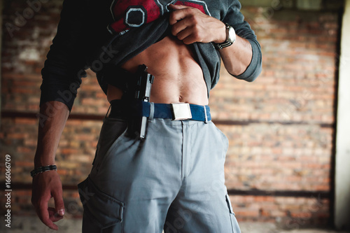 young athletic man holding a gun behind his belt.