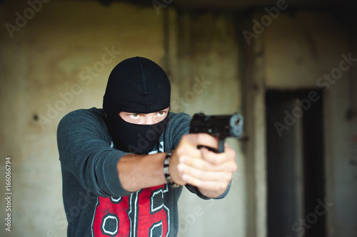 Athletic man in a balaclava, holds a pistol in his hand, is threatened with shooting, aiming