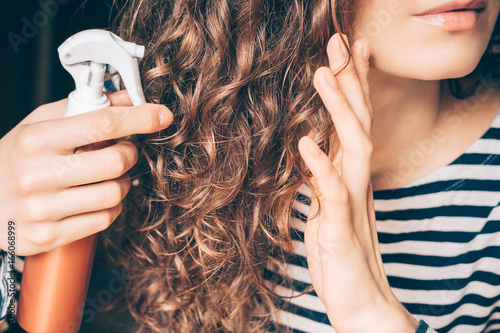 Woman applying spray on curly brown hair photo