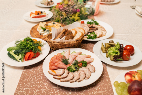 Cold meat plate with delicious sliced ham, prosciutto, meat and vegetables on celebratory dinner table in blur, selective focus. Meat platter with selection on wedding banquet