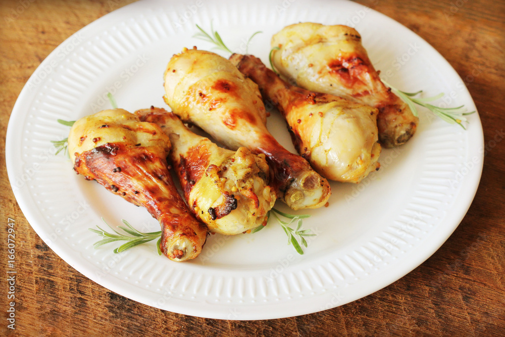 Grilled chicken legs with mustard on wooden table served on white plate with rosemary. BBQ dinner background Grilled chicken legs with mustard on wooden table served on white plate with rosemary. BBQ dinner background