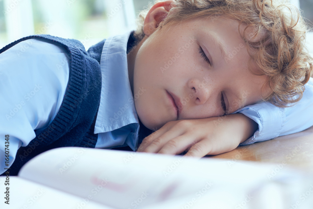 Tired schoolboy sleeping in classroom at school Tired schoolboy sleeping in classroom at school