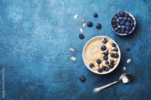 Bowl of oatmeal porridge with banana and blueberry on vintage table top view in flat lay style. Healthy breakfast and diet food. photo