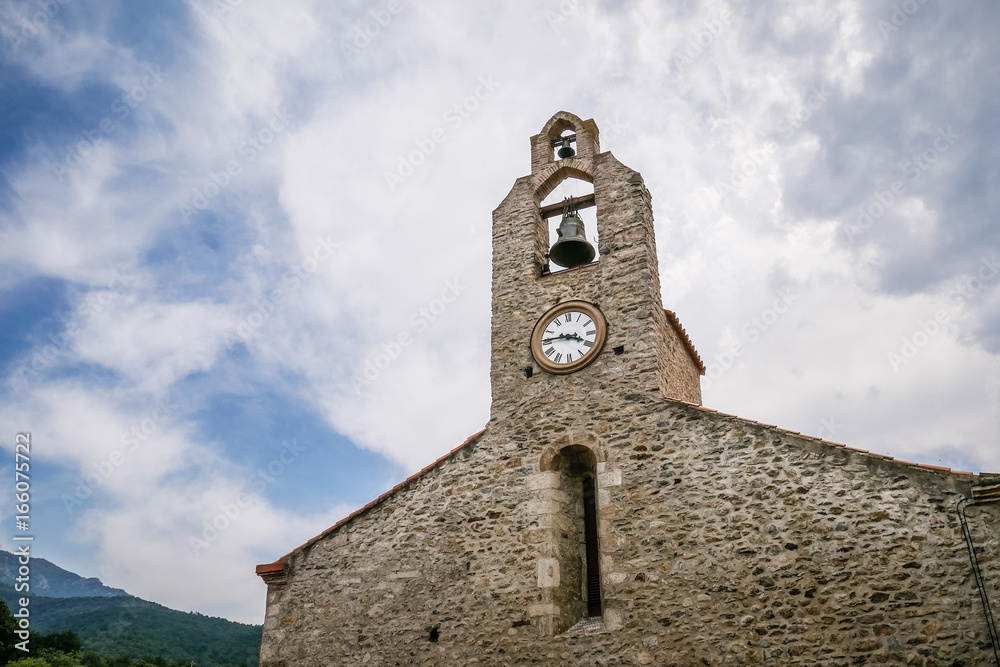Picturesque medieval stone church in south of France at traditional catalan village of Laroque des Albères, beautiful bell tower with cloudy sky background