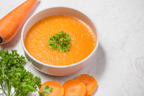 Carrot soup with cream and parsley on white stone background. Top view. Copy space photo