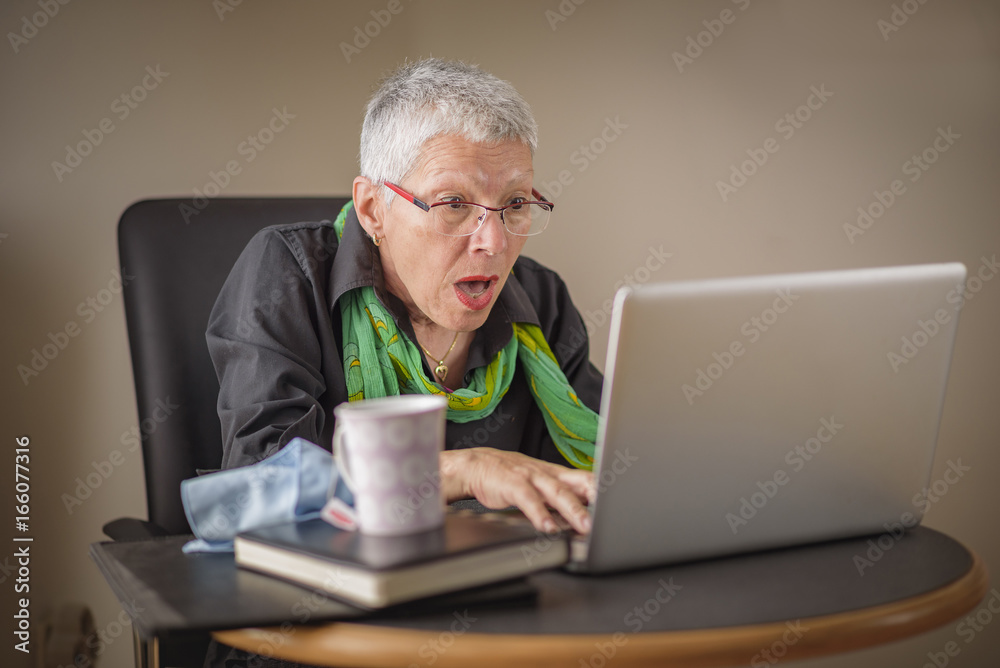 Senior business woman shocked with the content she finds on her laptop Senior business woman shocked with the content she finds on her laptop