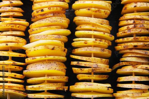Сырой желтый картофель в кожуре, порезанный на кусочки. Кусочки нанизаны на деревянные шпажки и приготовлены для запекания. 