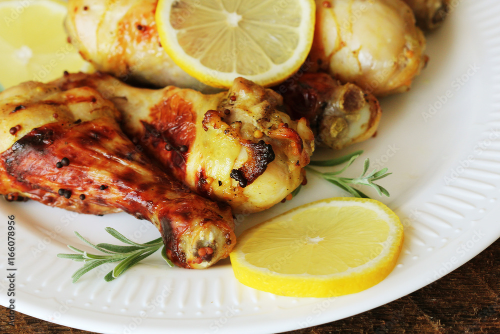 Grilled chicken legs with mustard on wooden table served on white plate with rosemary. BBQ dinner background Grilled chicken legs with mustard on wooden table served on white plate with rosemary. BBQ dinner background