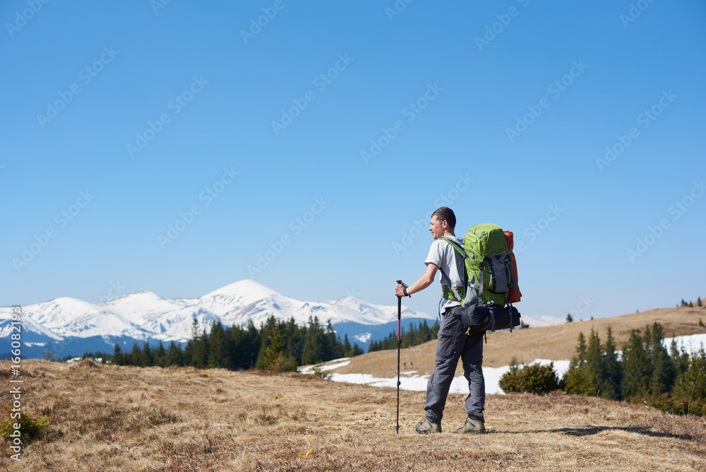 Rearview of an adventurous man with hiking equipment using trekking sticks while walking the mountain copyspace travelling adventure nature landscape sport activity