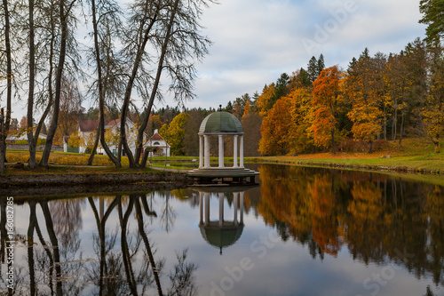 Gazebo (rotunda) on the shore of pond with other resindential buildings. Estonian manor. Autumn time.