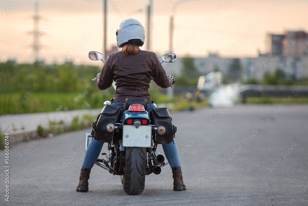 Fototapeta premium Beautiful woman a motorcycle driver waiting on the road at the evening, rear view