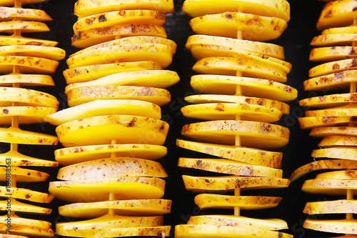 Сырой желтый картофель в кожуре, порезанный на кусочки. Кусочки нанизаны на деревянные шпажки, выложены в горизонтальный четыре ряда и подготовлены для дальнейшей готовки.