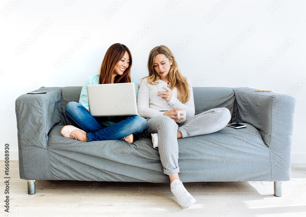 Tow young women using technology devices sitting on a sofa Tow young women using technology devices sitting on a sofa