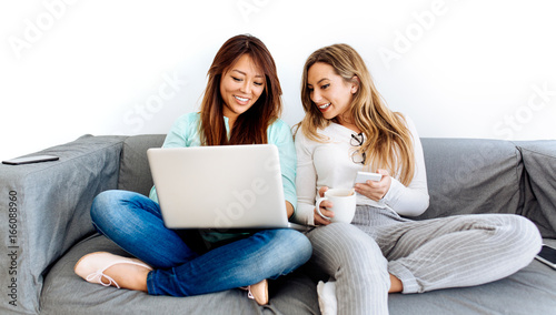 Tow young women using technology devices sitting on a sofa