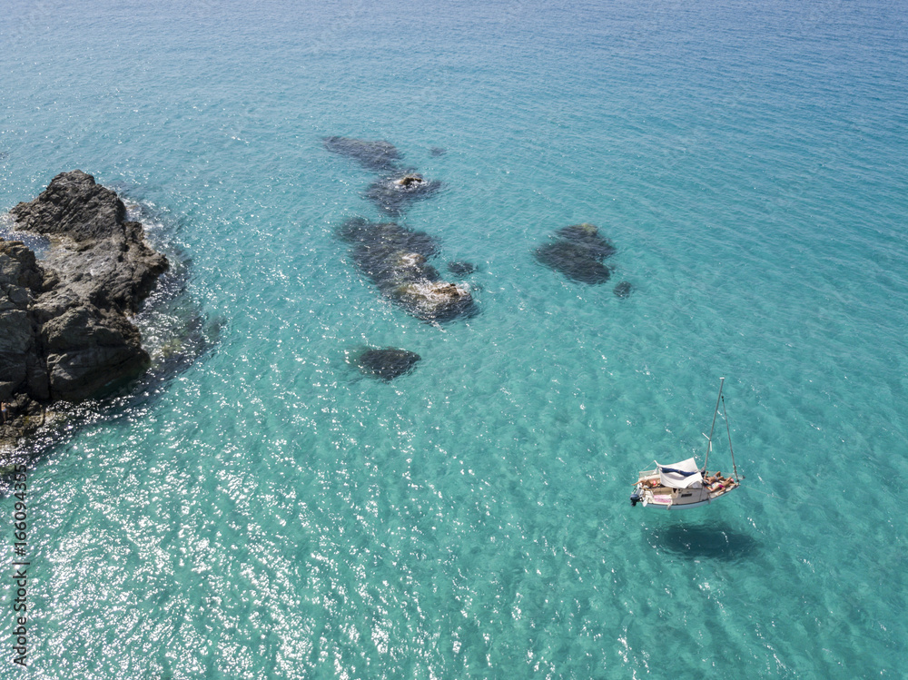 Obraz premium Vista aerea di una barca ormeggiata che galleggia su un mare trasparente. Immersioni relax e vacanze estive. Coste italiane, spiagge e rocce