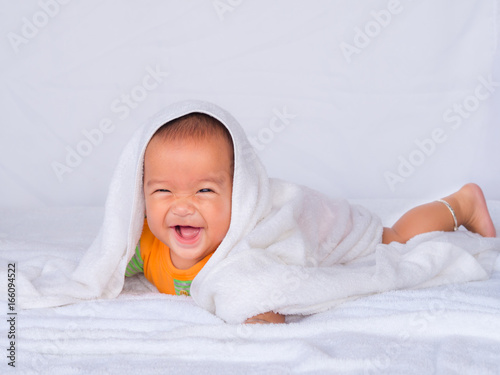Asian infant lie on the stomach, Wearing an orange shirt On a white cloth. under a white towel.