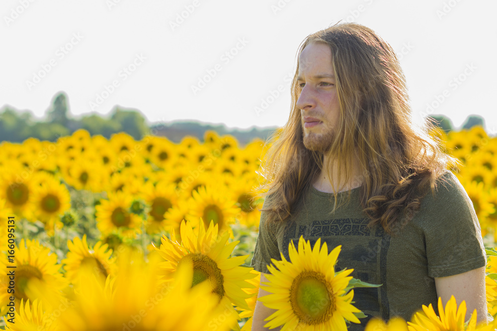 Young caucasian - nordic man with blond and long hairs at sunflowers field Young caucasian - nordic man with blond and long hairs at sunflowers field