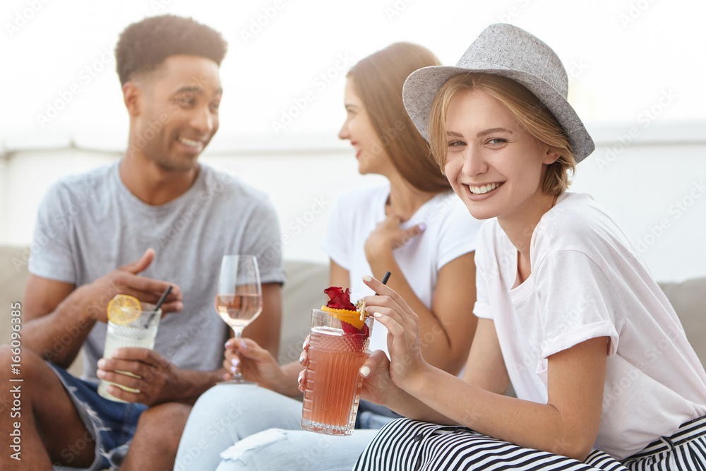 Group of happy young people toasting to love and prosperity, having alcohol drinks at rooftop party. Three cheerful friends enjoying nice time together, having fun at terrace cafe, drinking cocktails Group of happy young people toasting to love and prosperity, having alcohol drinks at rooftop party. Three cheerful friends enjoying nice time together, having fun at terrace cafe, drinking cocktails