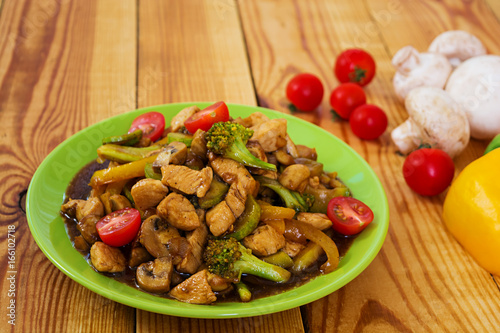 Stir fry chicken, zucchini and broccoli on wooden background