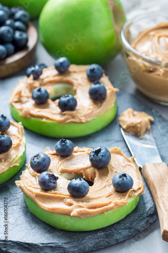 Green apple rounds with peanut butter and blueberries on slate board, vertical