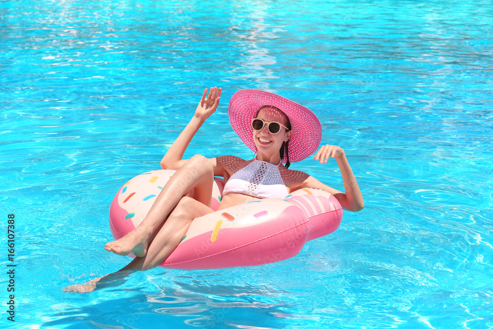 Beautiful young woman with inflatable donut in blue swimming pool
