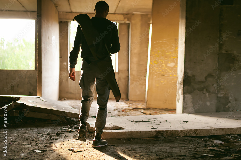 Athletic man walks through the ruins, with a cover for a gun for weeping, warm rays of light in the window Athletic man walks through the ruins, with a cover for a gun for weeping, warm rays of light in the window